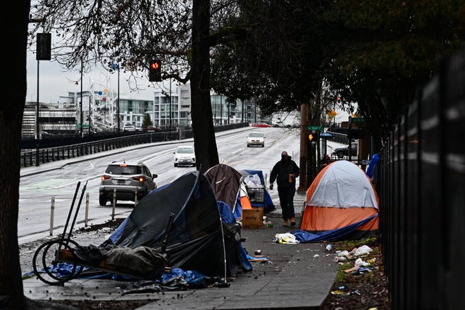 A pedestrian walks past an encampment of tents after crossing Hoyt Street in Portland, Ore. on Jan. 24, 2024.
