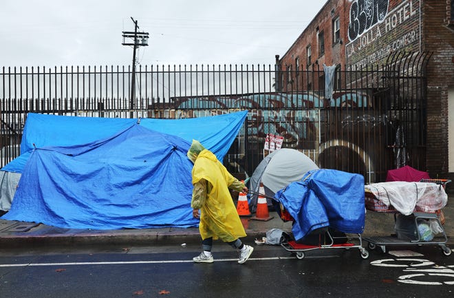 A person walks with carts in the rain near an encampment of unhoused people in Skid Row as a powerful long-duration atmospheric river storm, the second in less than a week, impacts Southern California on Feb. 6, 2024 in Los Angeles.