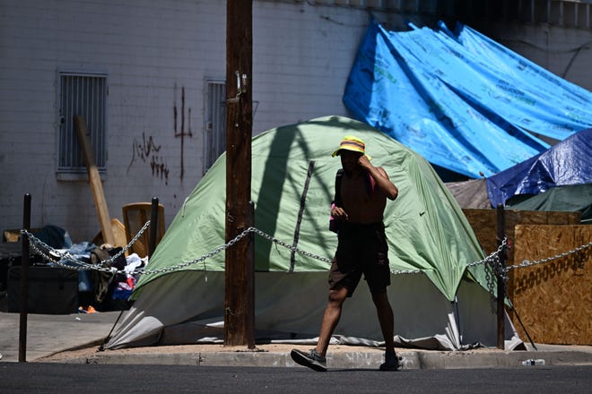 A person walks past tents in "The Zone," a vast homeless encampment where hundreds of people reside, during a record heat wave in Phoenix on July 18, 2023.