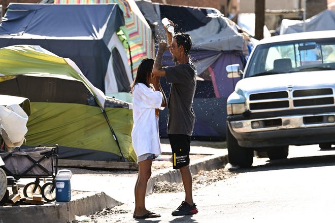 Roni and John pour water on themselves to cool off from extreme heat while residing in "The Zone," a vast homeless encampment where hundreds of people reside, during a record heat wave in Phoenix, Arizona. on July 19, 2023.