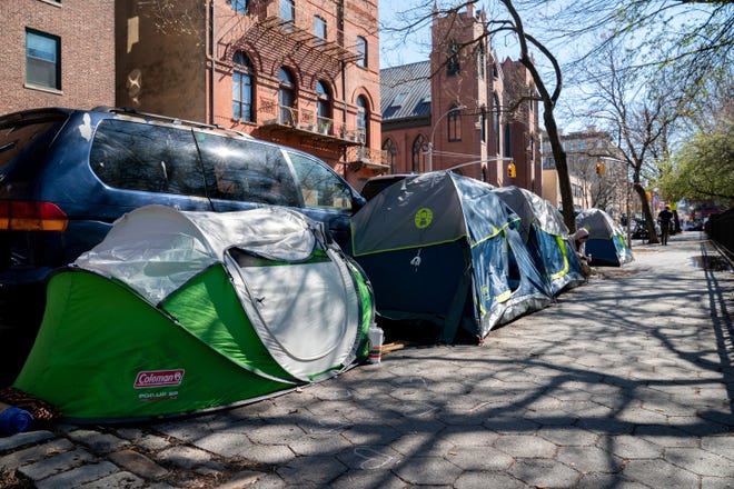 A person sits between tents belonging to homeless people who were removed from an encampment on East 9th Street earlier this week and have relocated a block adjacent to Tompkins Square Park in New York City, April 8, 2022.